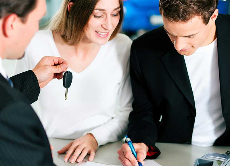 a man signing a document next to a woman holding car keys